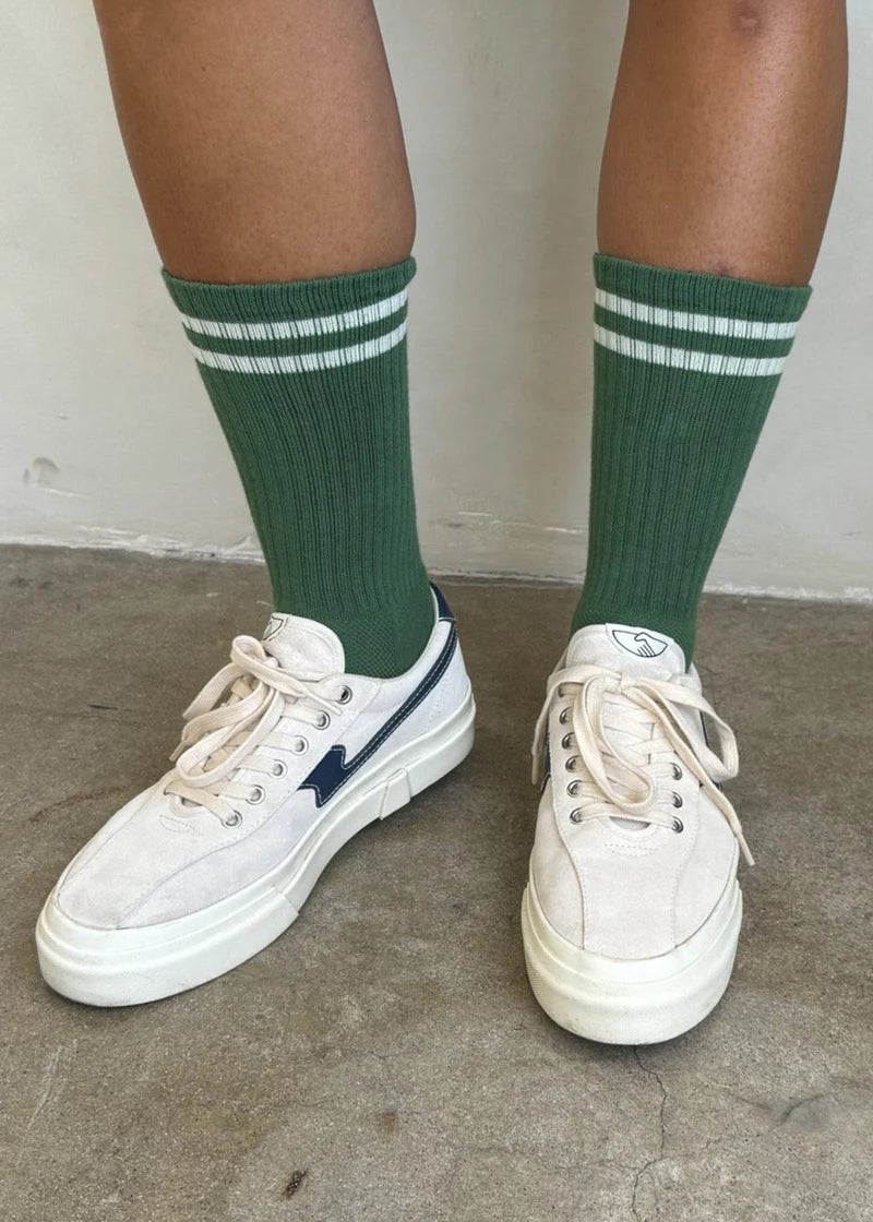 Person wearing green socks with white stripes and white tennis shoes on concrete floor