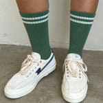 Person wearing green socks with white stripes and white tennis shoes on concrete floor