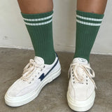 Person wearing green socks with white stripes and white tennis shoes on concrete floor