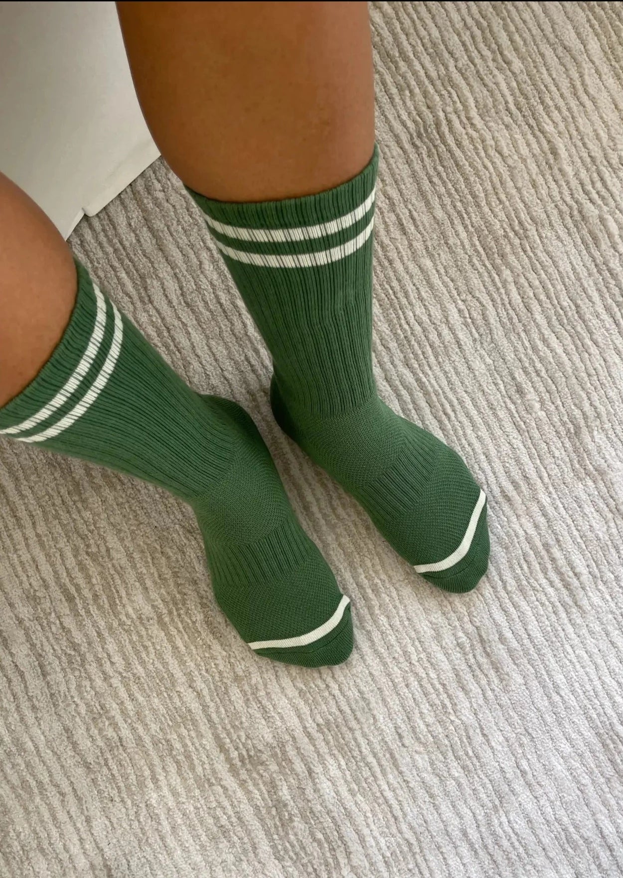 Person wearing green socks with white stripes on carpet floor