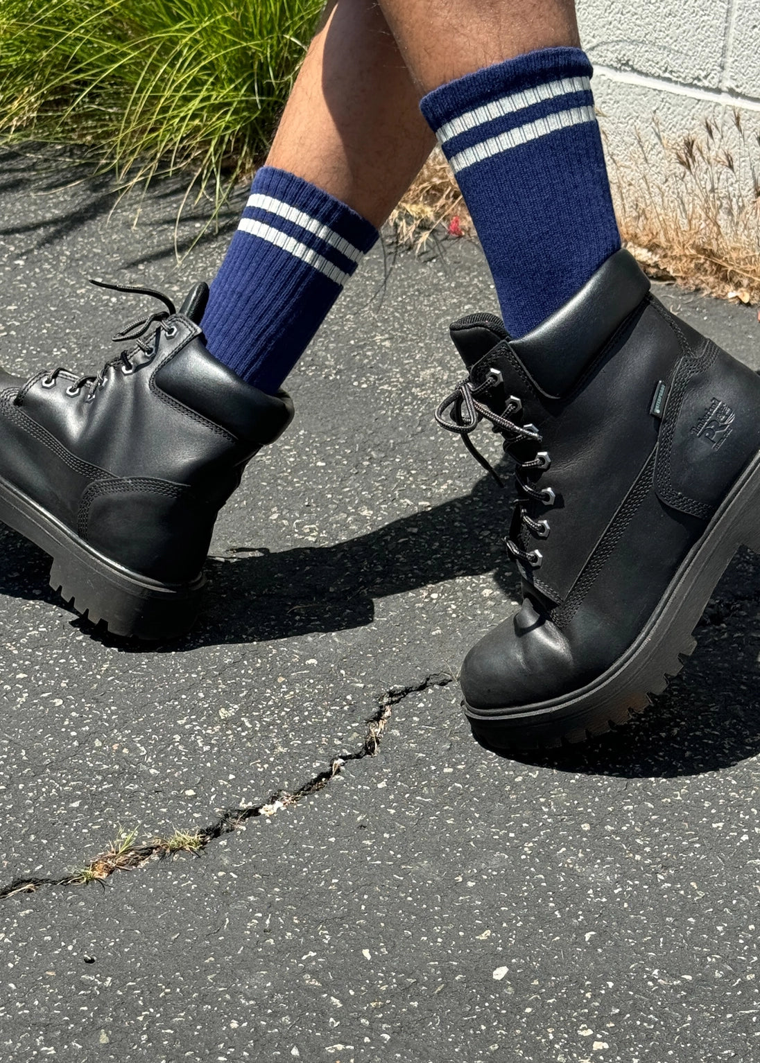 Person wearing navy socks with white stripes and black lace up boots walking on concrete