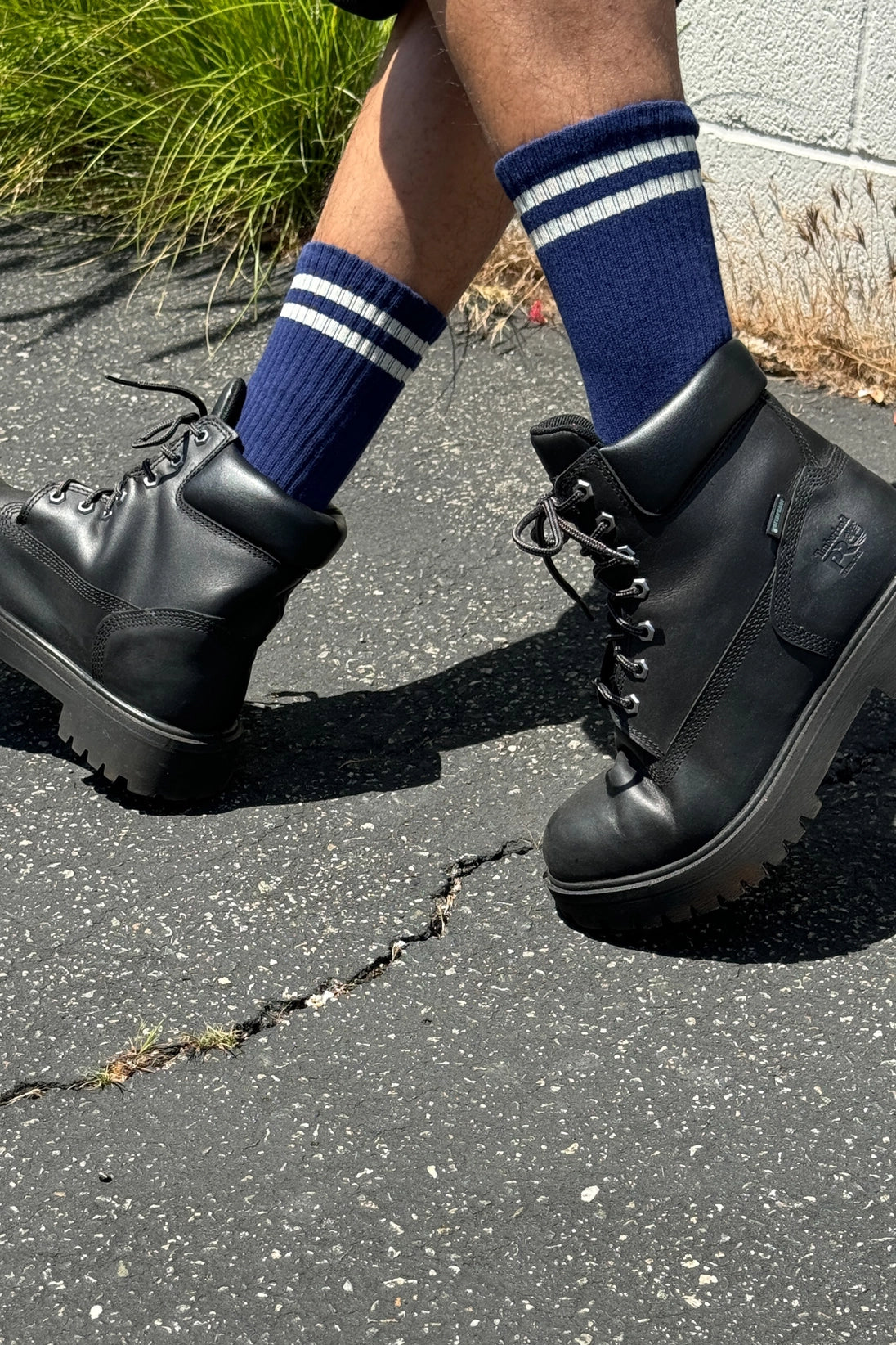 Person wearing navy socks with white stripes and black lace up boots walking on concrete