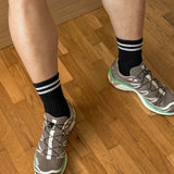 A pair of black calf-length socks with white stripes on the cuff, worn with sneakers.