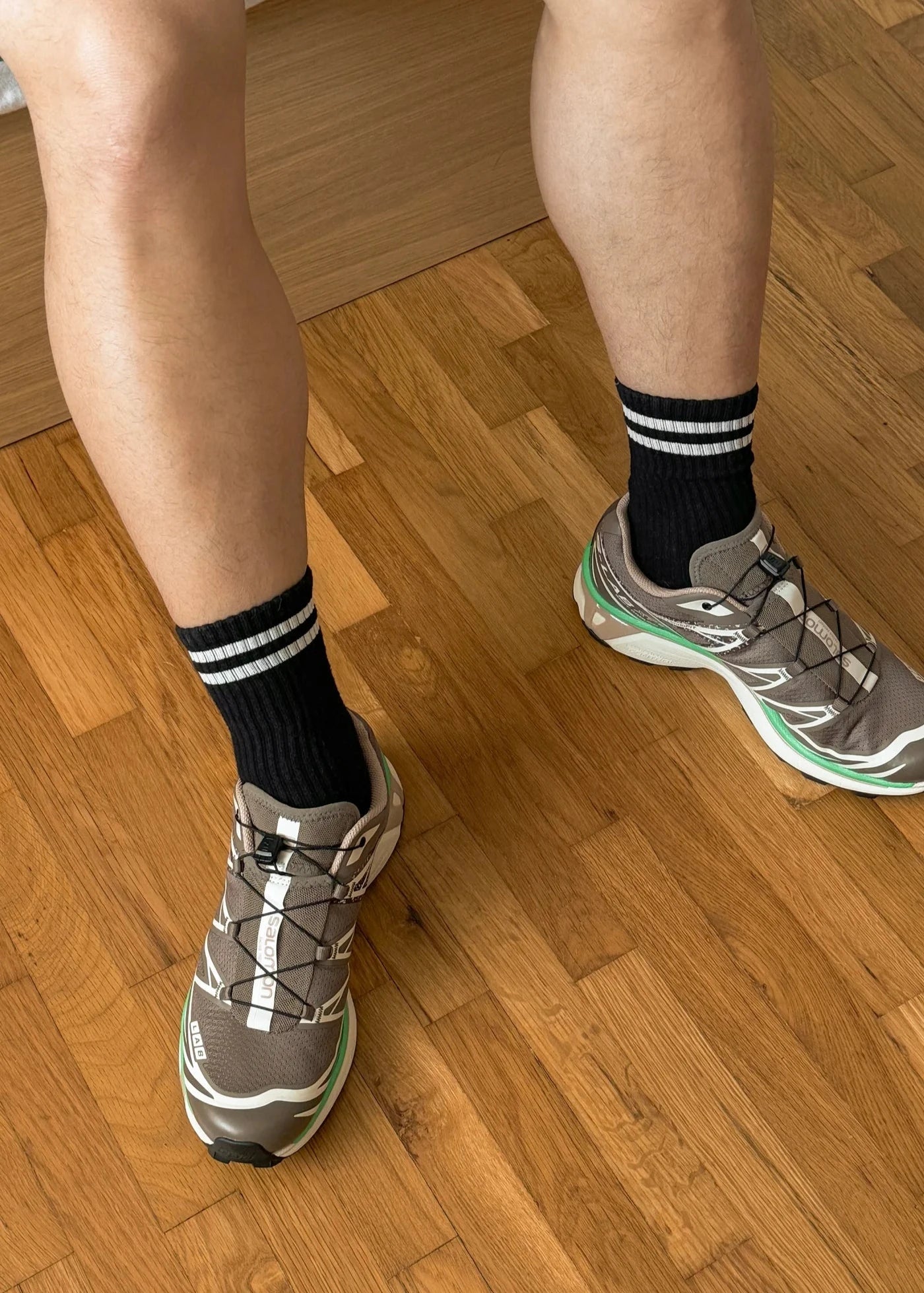 A pair of black calf-length socks with white stripes on the cuff, worn with sneakers.