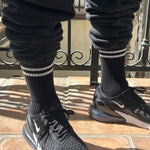 Person wearing black socks with white stripes black sweat pants and black sneakers on a tile floor