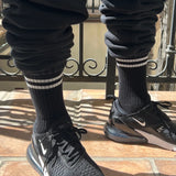 Person wearing black socks with white stripes black sweat pants and black sneakers on a tile floor
