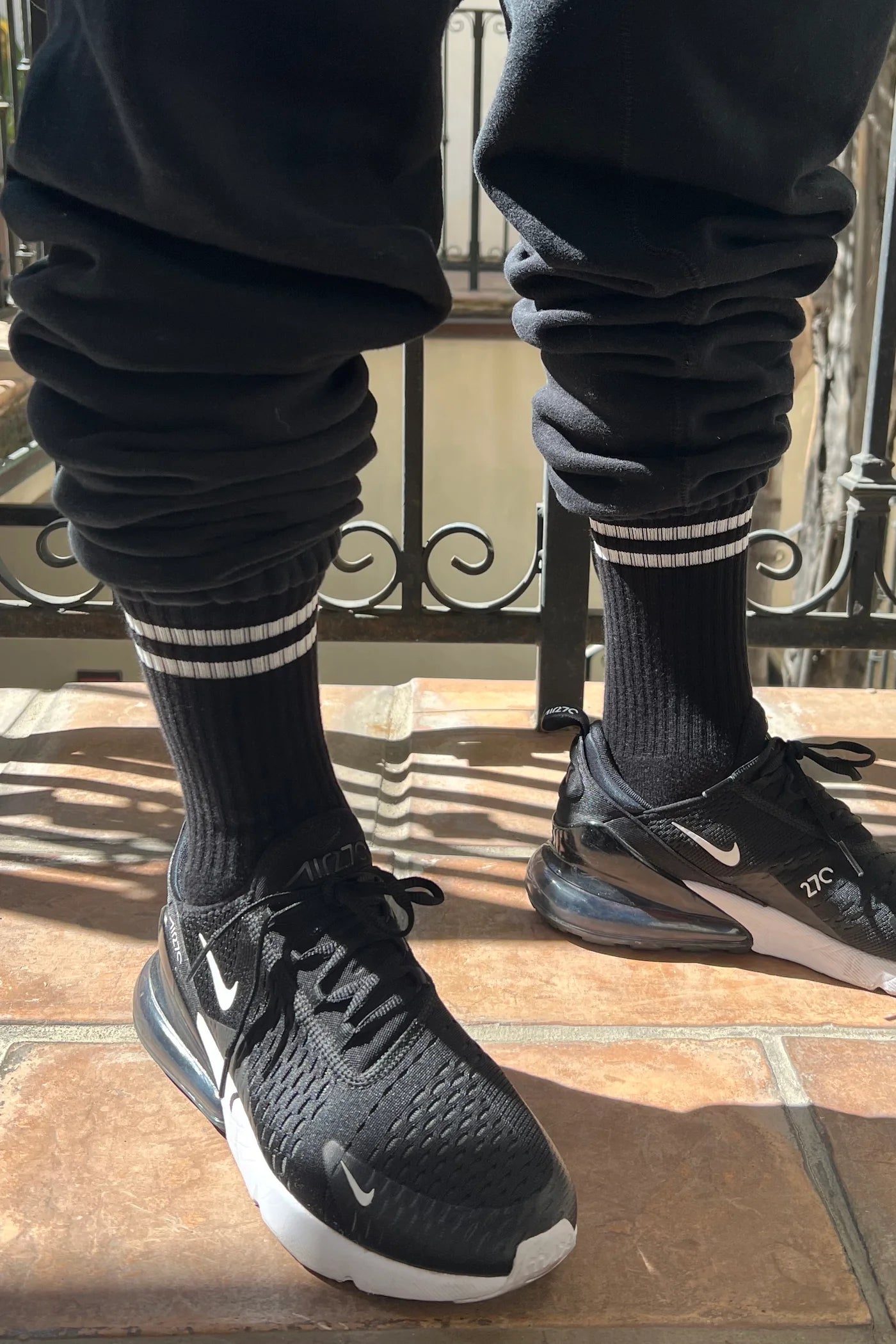 Person wearing black socks with white stripes black sweat pants and black sneakers on a tile floor