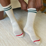 White socks with green stripes and red accents worn by a person sitting on a textured surface.