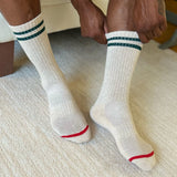 White socks with green stripes and red accents worn by a person sitting on a textured surface.