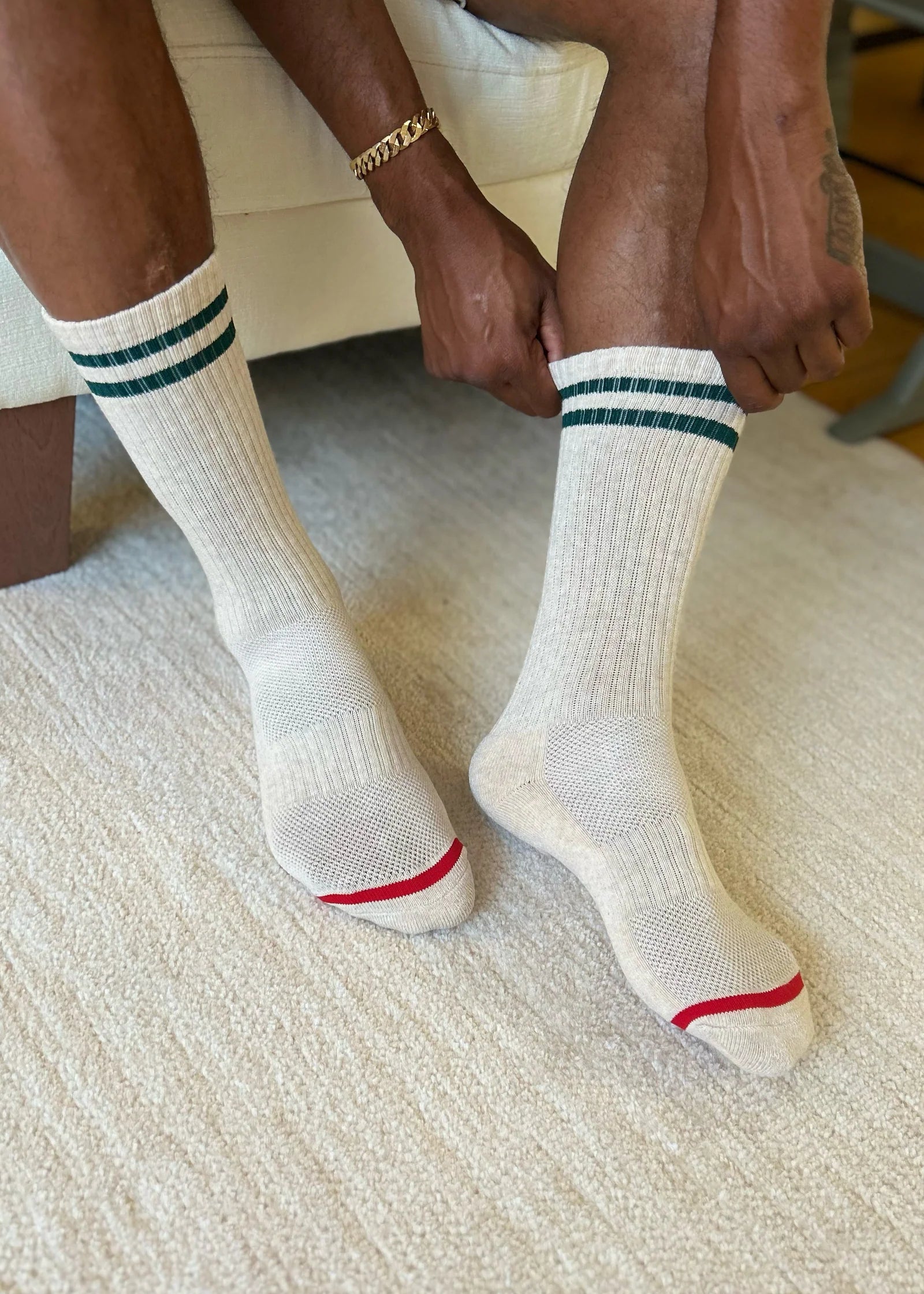 White socks with green stripes and red accents worn by a person sitting on a textured surface.