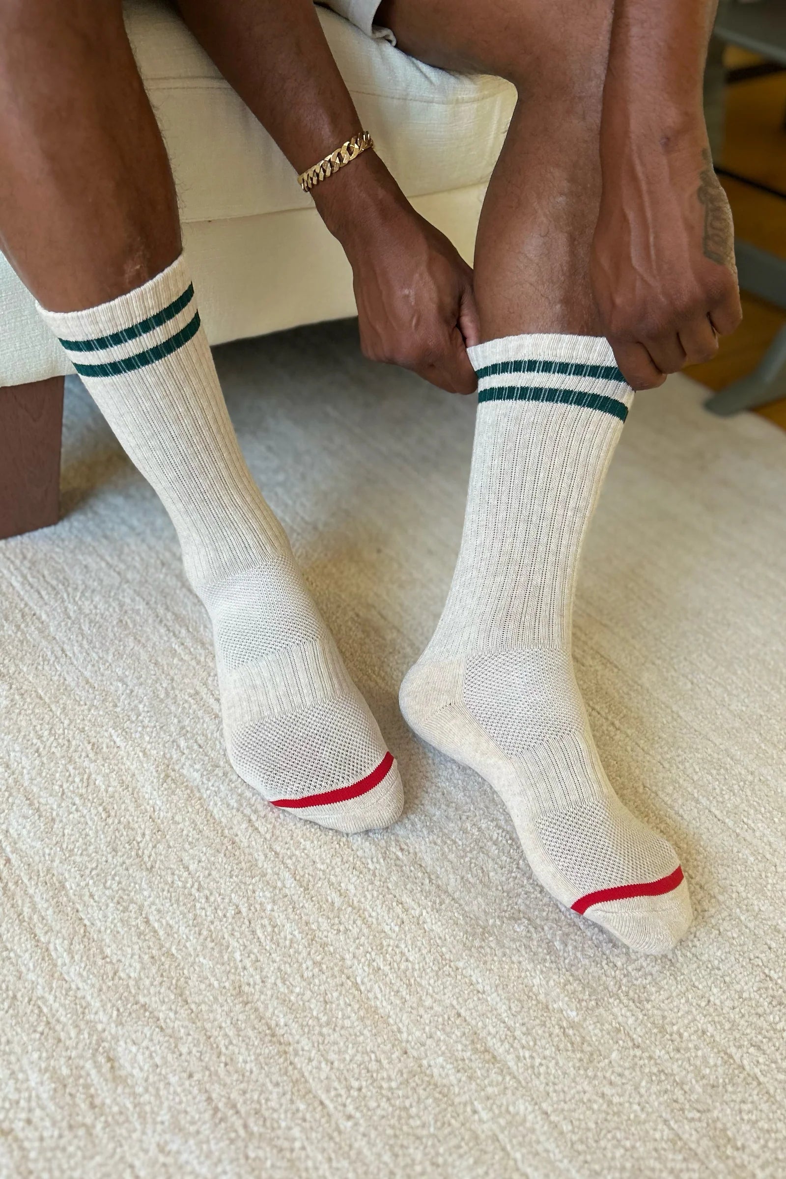 White socks with green stripes and red accents worn by a person sitting on a textured surface.