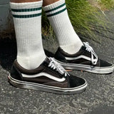 Person wearing white socks with green socks and black sneakers on concrete
