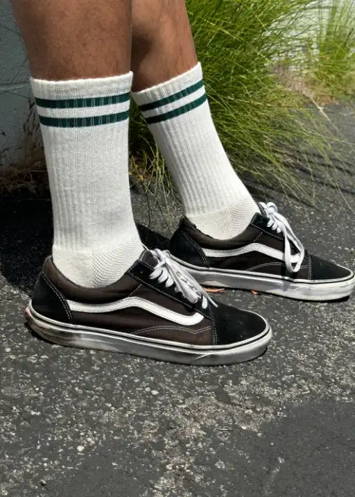 Person wearing white socks with green socks and black sneakers on concrete
