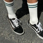 Person wearing white socks with green stripes and black sneakers on concrete