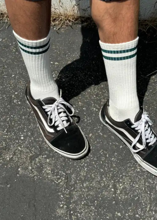 Person wearing white socks with green stripes and black sneakers on concrete