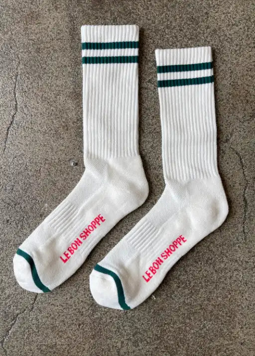 White socks with green stripes and red Le Bon Shoppe branding laying on concrete flooring