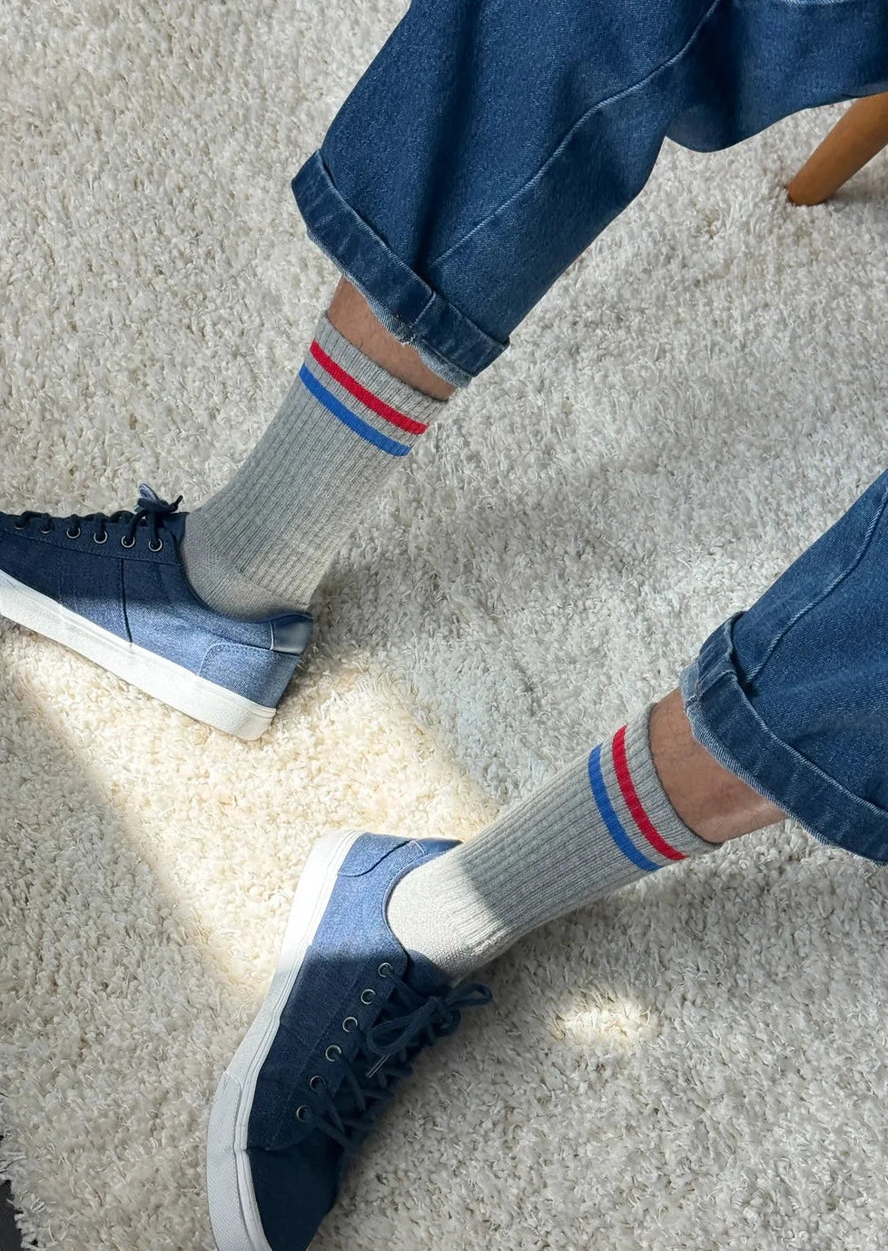 A pair of grey socks with red and blue stripes on the cuffs, worn with blue jeans and blue sneakers.