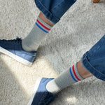 A pair of grey socks with red and blue stripes on the cuffs, worn with blue jeans and blue sneakers.