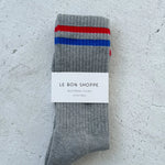 Grey socks with red and blue stripes in white Le Bon Shoppe packaging on white background