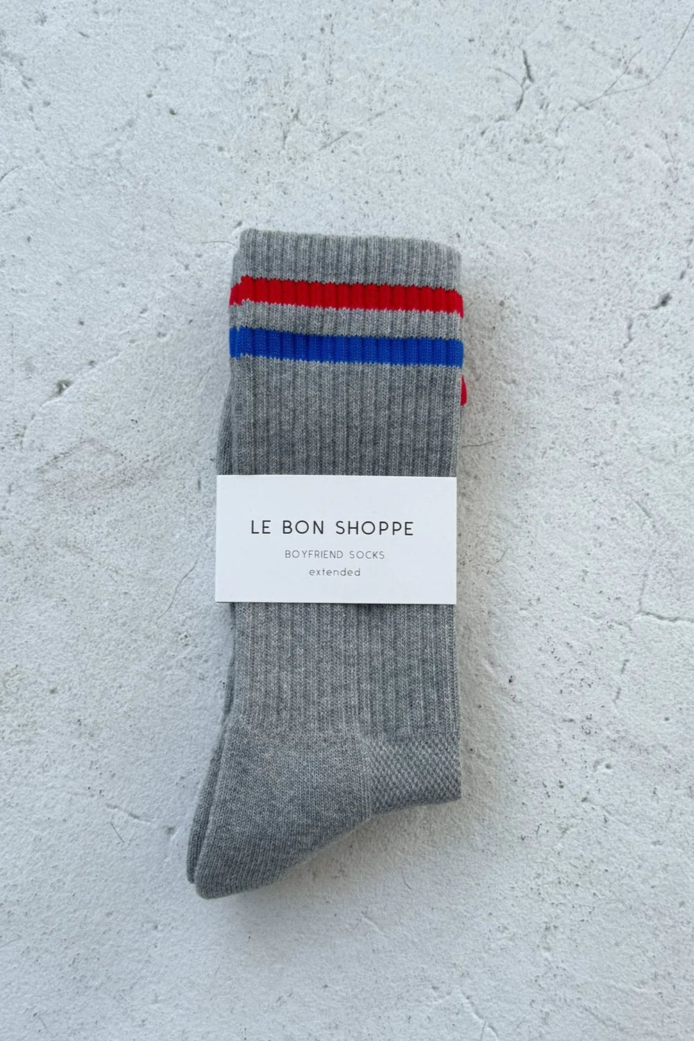 Grey socks with red and blue stripes in white Le Bon Shoppe packaging on white background