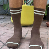 Brown socks with white stripes worn by a person on a brick pavement.