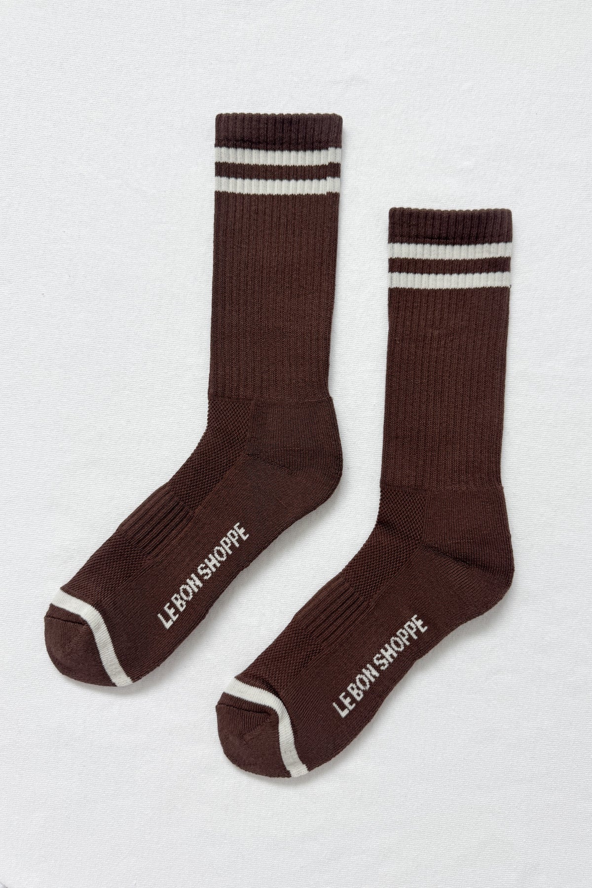 Pair of brown socks with white stripes and 'Le Bon Shoppe' branding on a light gray background