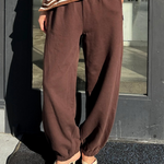 Person wearing brown striped shirt and brown pants standing in front of a glass door.