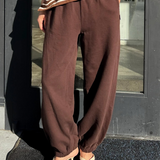 Person wearing brown striped shirt and brown pants standing in front of a glass door.