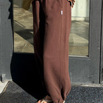 Person wearing brown sweatpants and a striped shirt standing in front of a glass door.