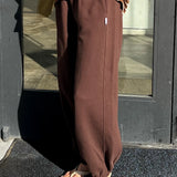 Person wearing brown sweatpants and a striped shirt standing in front of a glass door.
