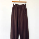 Brown pants hanging on a wooden hanger against a white wall
