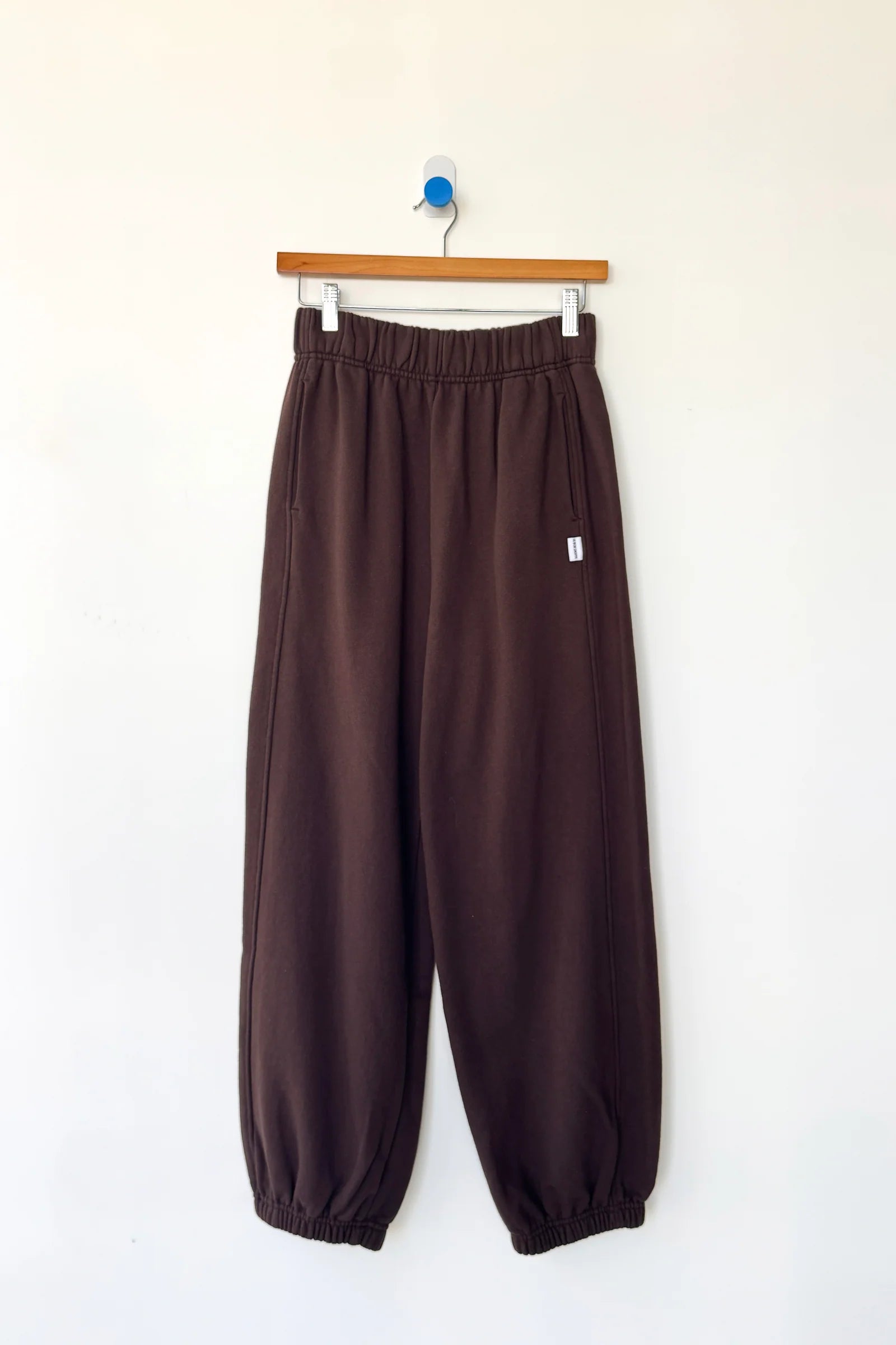 Brown pants hanging on a wooden hanger against a white wall