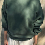 Person wearing a green sweatshirt and white pants against a concrete wall.