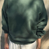 Person wearing a green sweatshirt and white pants against a concrete wall.