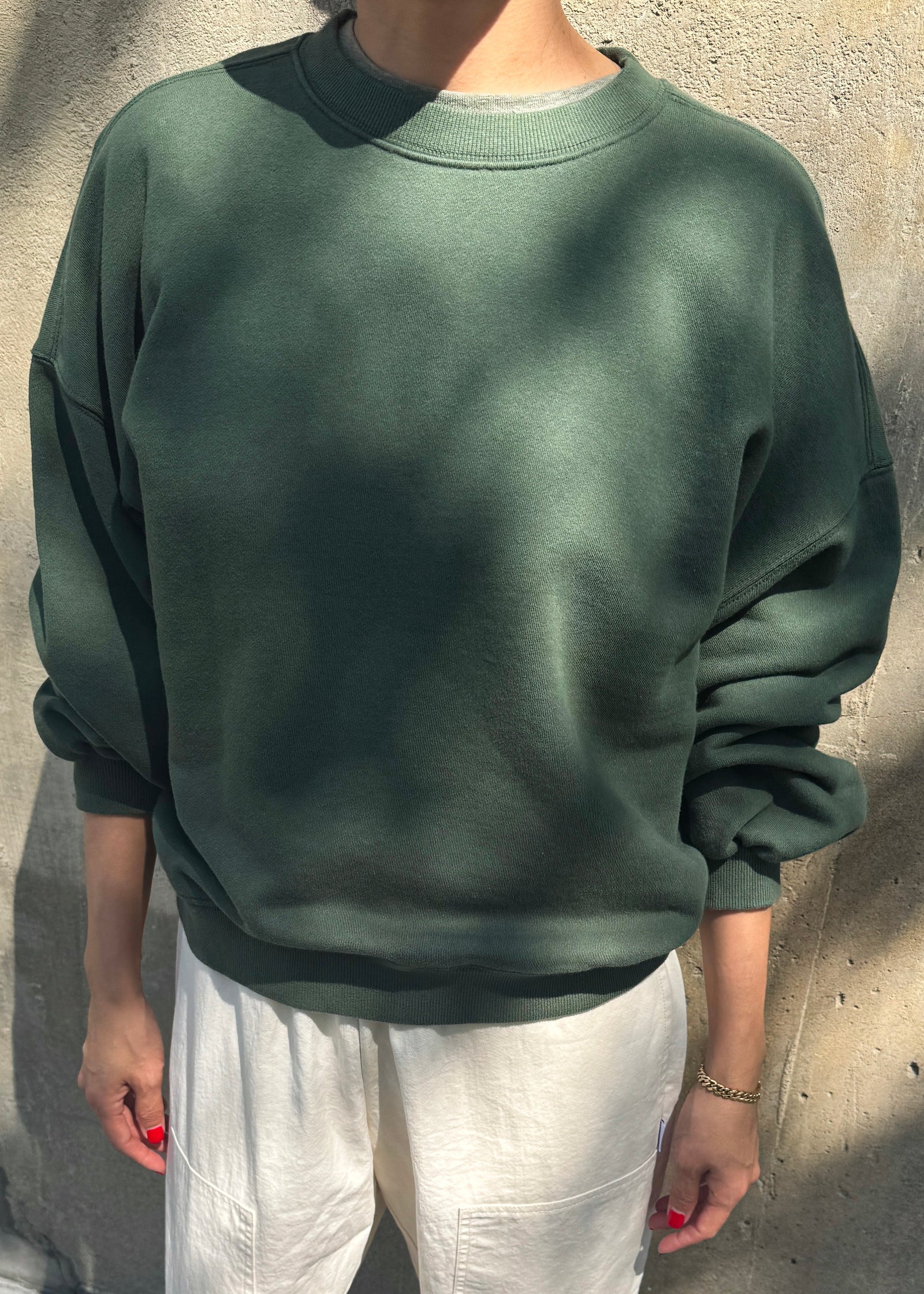 Person wearing a green sweatshirt and white pants against a concrete wall.