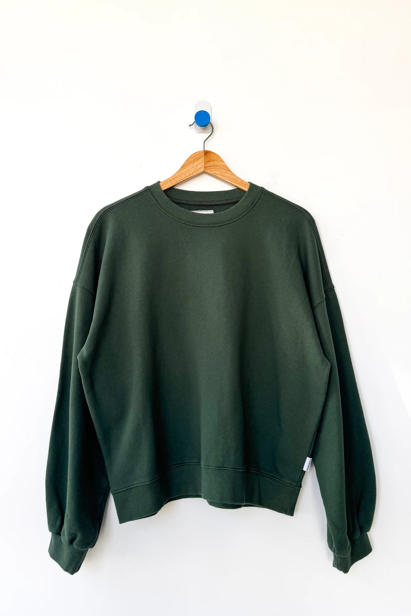 Green sweatshirt on a wooden hanger against a white background