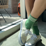 Person wearing white sneakers with green striped socks in a casual setting.