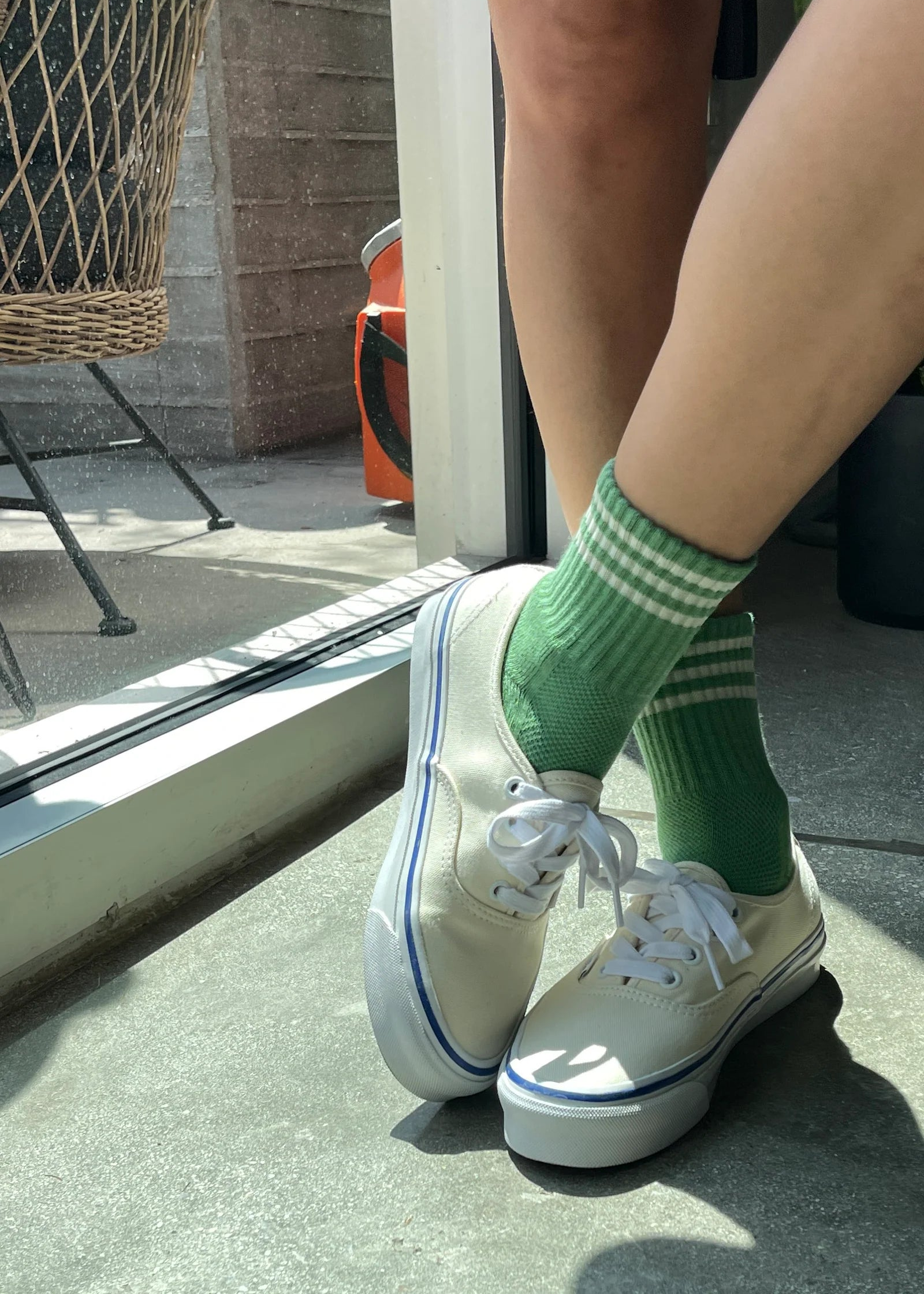 Person wearing white sneakers with green striped socks in a casual setting.