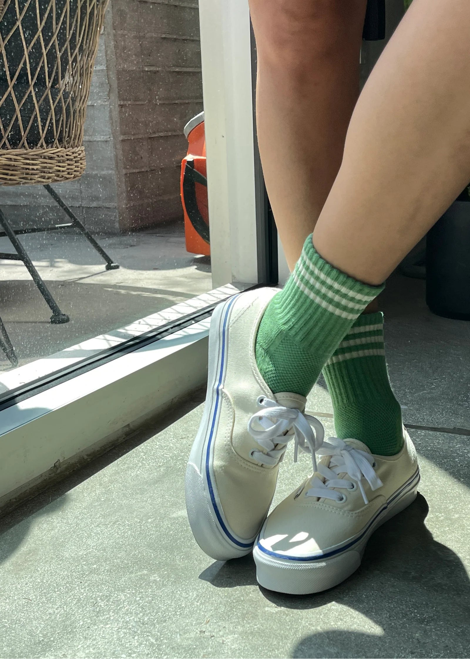 Person wearing white sneakers with green striped socks in a casual setting.
