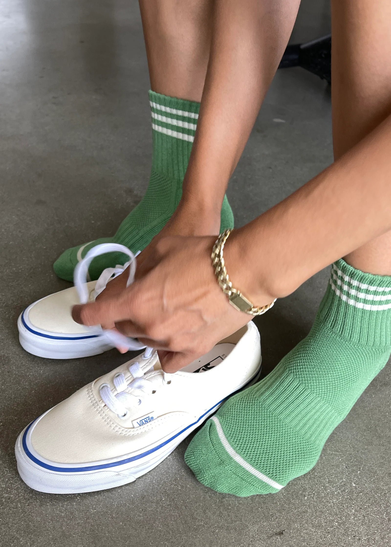 Person wearing green socks with white stripes and white sneakers on a concrete floor.