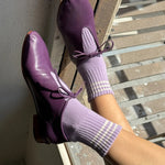 Purple shoes and socks on a person standing on a wooden floor.