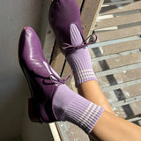 Purple shoes and socks on a person standing on a wooden floor.