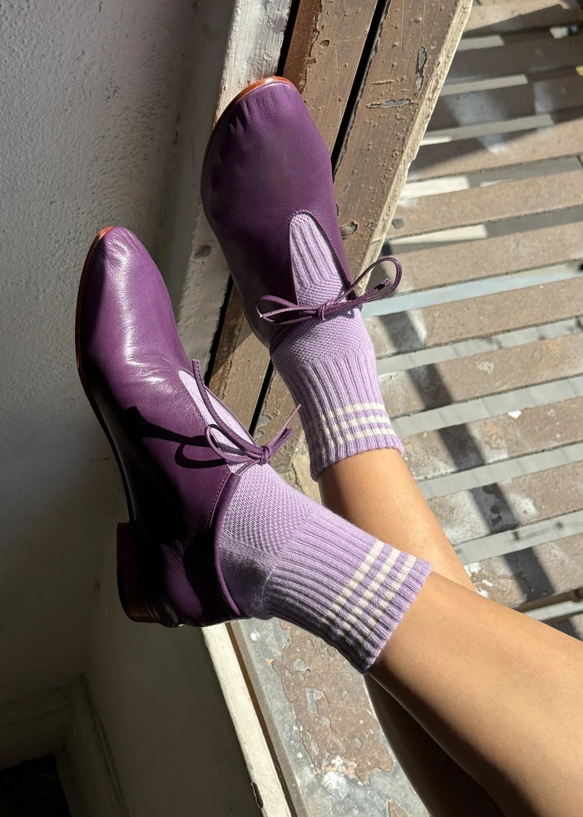 Purple shoes and socks on a person standing on a wooden floor.