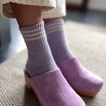 Purple clogs worn with striped socks on a textured floor.