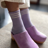 Purple clogs worn with striped socks on a textured floor.