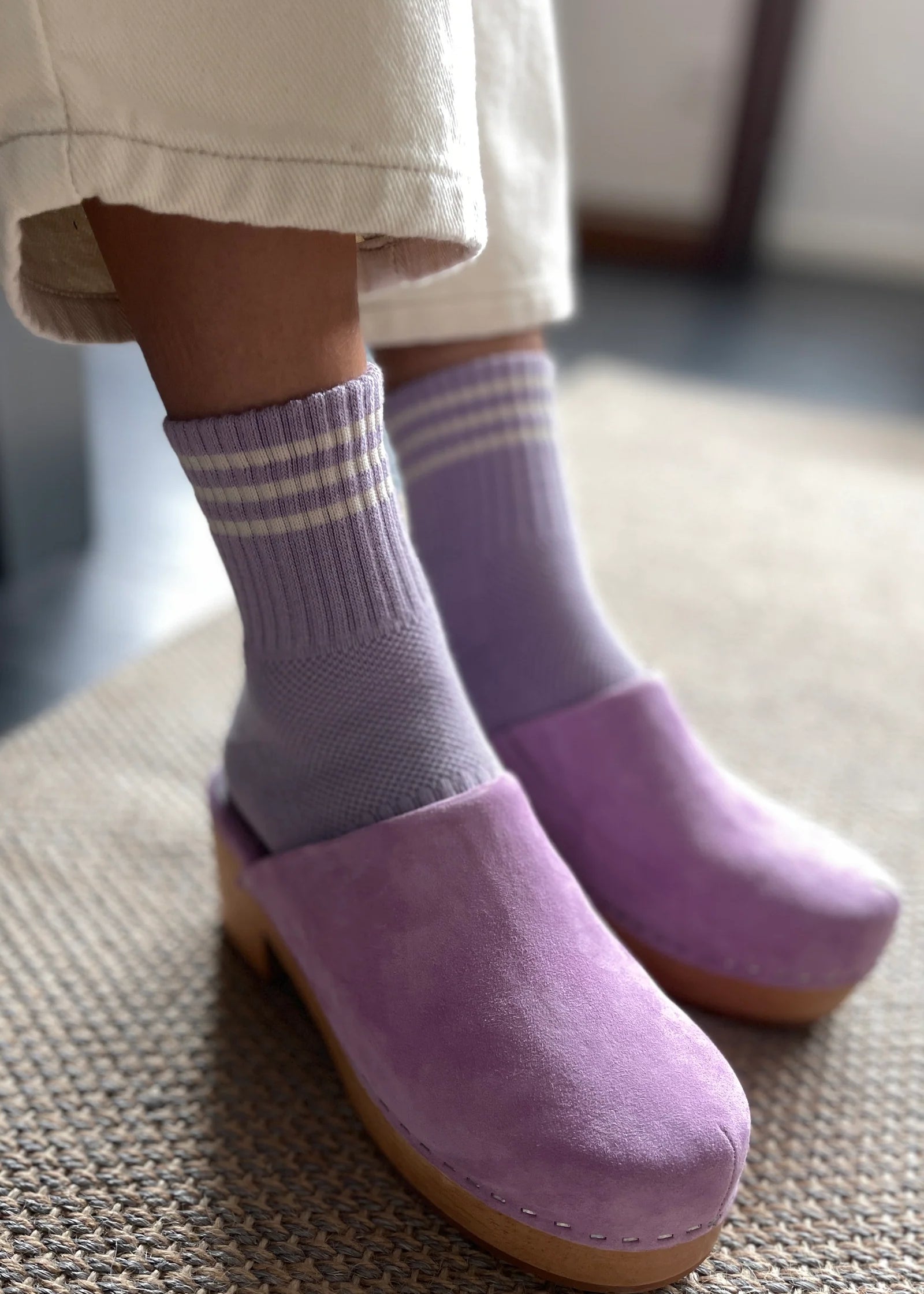 Purple clogs worn with striped socks on a textured floor.