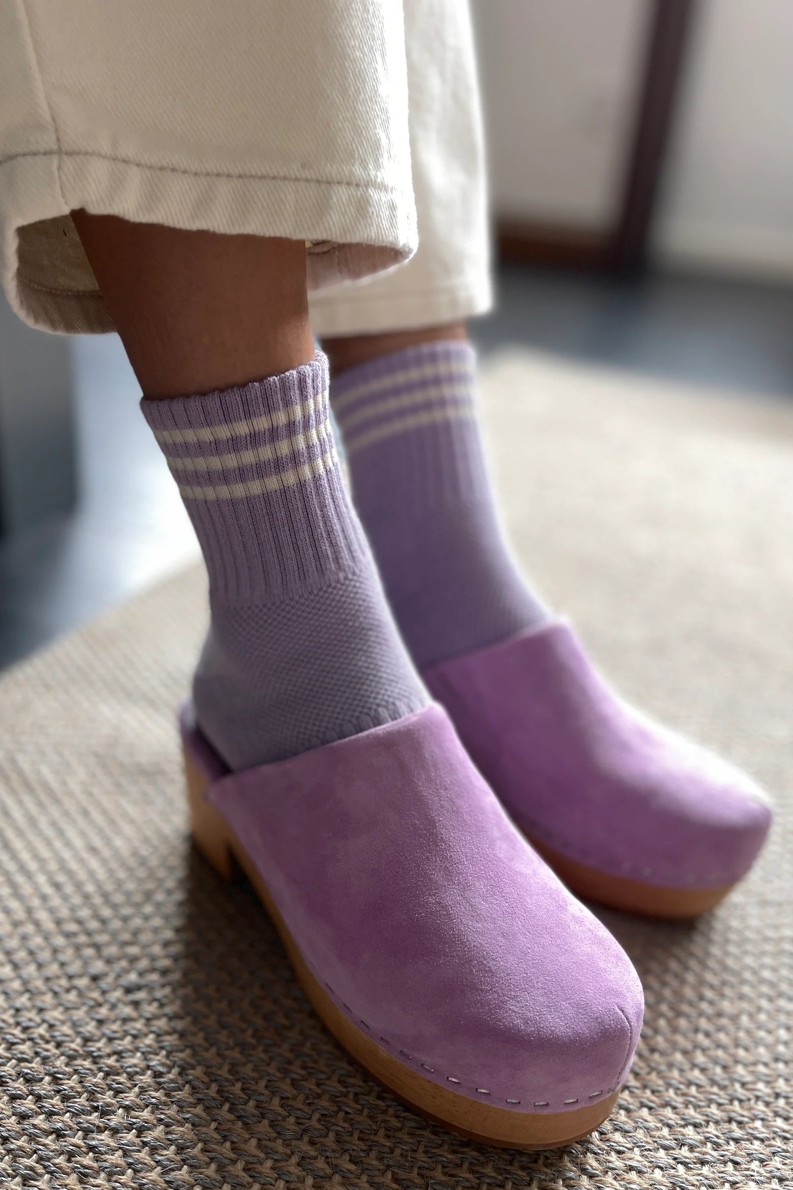 Purple clogs worn with striped socks on a textured floor.