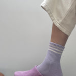 Person wearing purple clogs and striped socks on a plain background