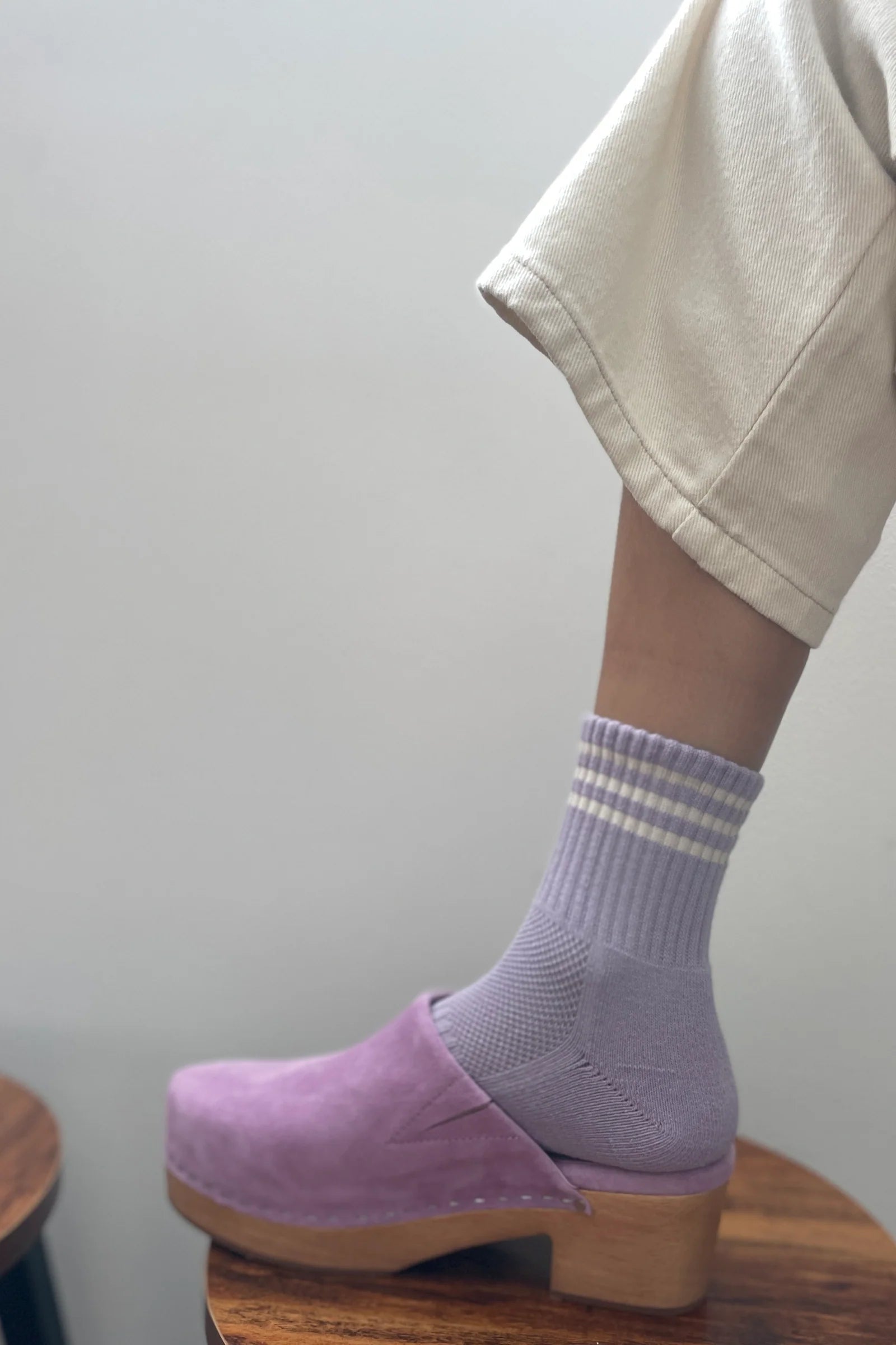 Person wearing purple clogs and striped socks on a plain background