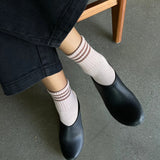 Person wearing black pants, pink socks with brown stripes and black shoes on concrete floor